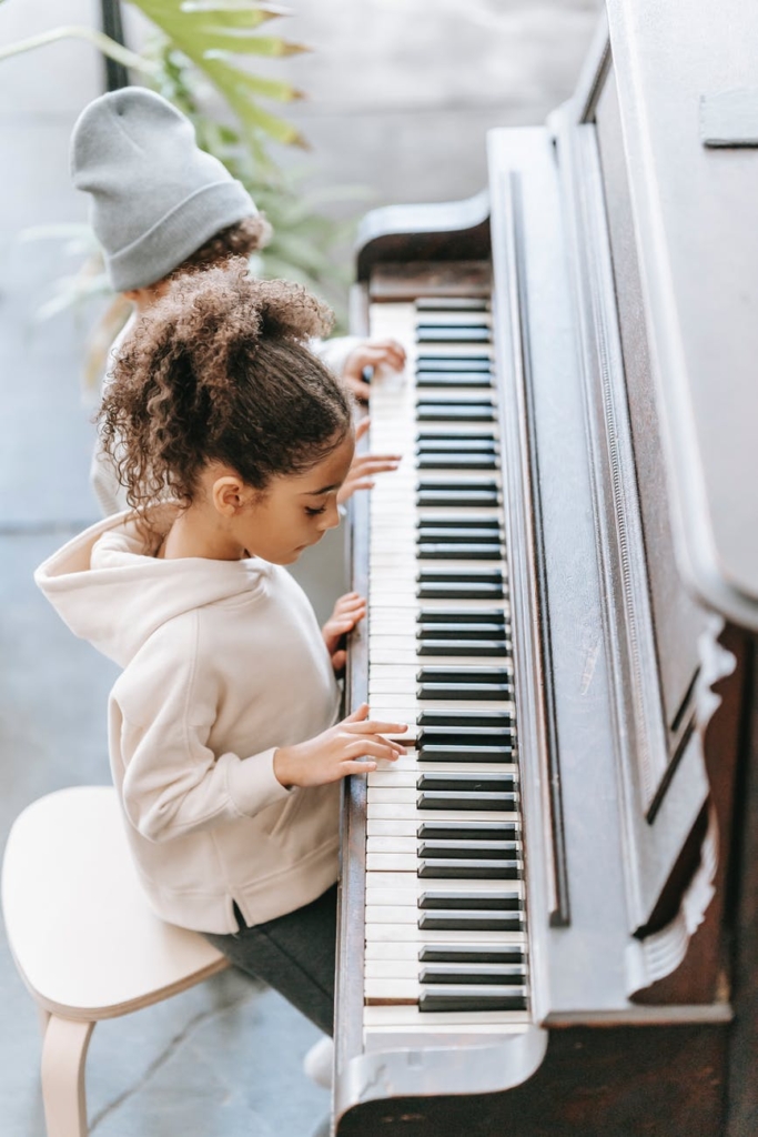 focused ethnic kid playing piano with sibling at home